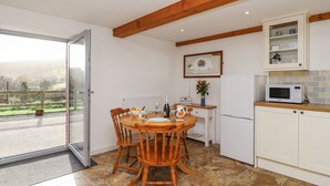 A kitchen with a dining table, chairs, a microwave, cabinets, and a view through a glass door. - Swallow Cottage (South Brent)