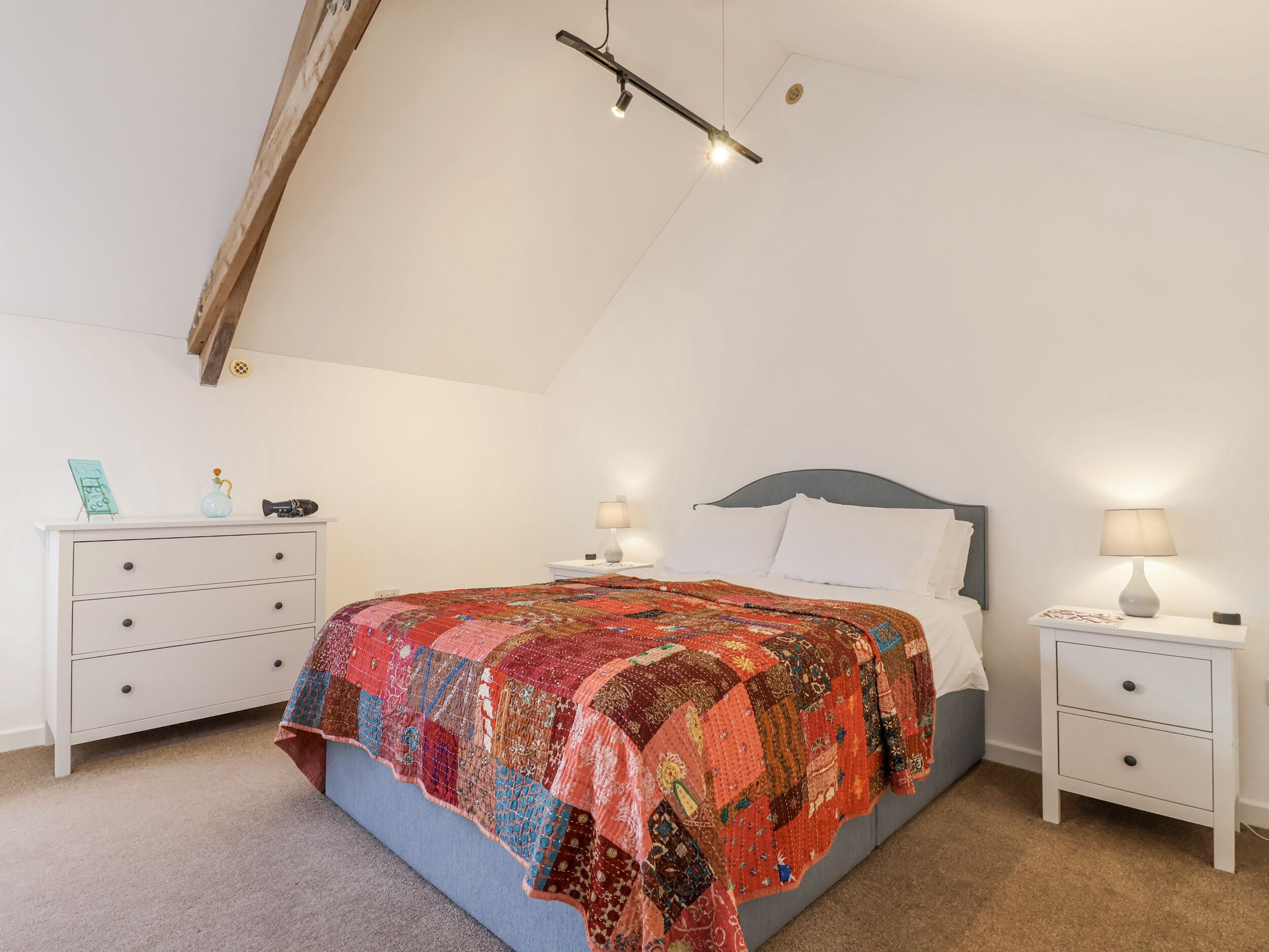 A bedroom with a bed, two bedside tables, a dresser, and a ceiling light fixture.