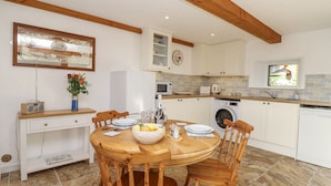 A modern kitchen with a dining area, featuring a wooden table, chairs, and a built-in washing machine. - Swallow Cottage (South Brent)