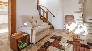 A living room with a beige sofa, a wooden coffee table, a patterned rug, a stone wall, and a staircase. - Swallow Cottage (South Brent)