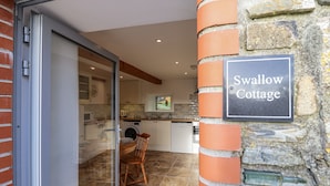 A modern kitchen with a stone wall and a sign reading "Swallow Cottage." - Swallow Cottage (South Brent)