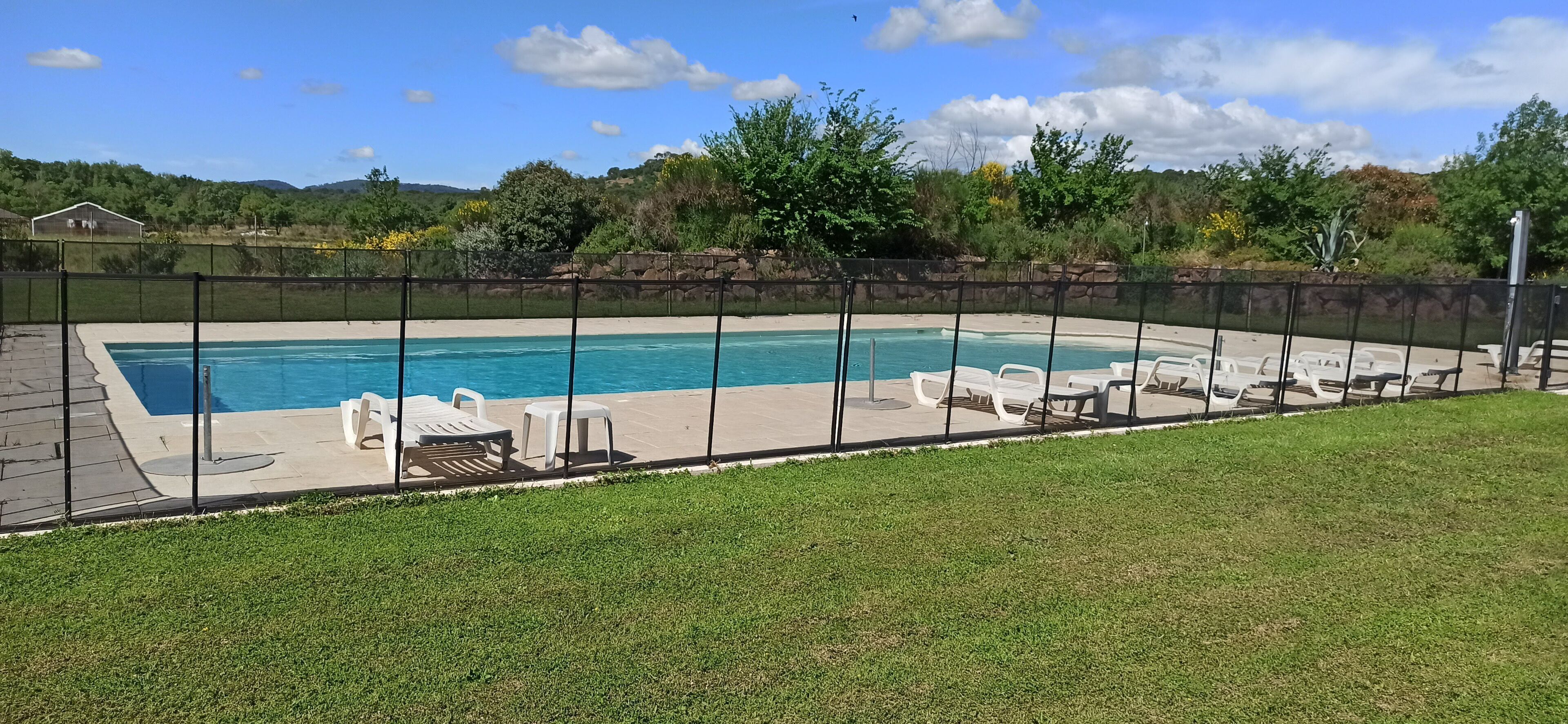 Ein rechteckiger Pool mit schwarzem Zaun, umgeben von weißen Liegestühlen und einer Rasenfläche.