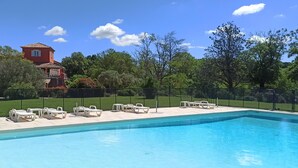 Piscina com espreguiçadeiras, um edifício vermelho e um gramado verde.
