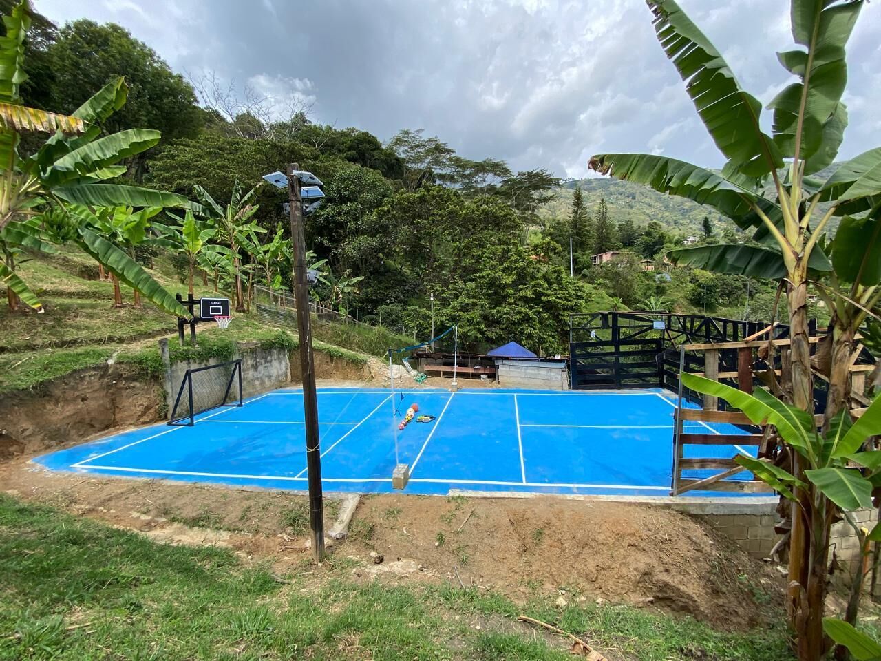 An outdoor basketball court surrounded by greenery and a wooden fence.