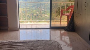 A room with a bed, a view of mountains through a glass door, and a red chair outside. - FARM WITH BEAUTIFUL VIEW 40MIN FROM MEDELLÍN. SPORTS COURT, SWIMMING POOL AND GYM. (Barbosa)