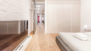 Une chambre moderne avec un plancher en bois, un lit recouvert de draps blancs, une télévision et une armoire.