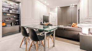 Un espace repas moderne avec une table et des chaises en verre, un meuble à vin intégré et un coin salon confortable avec un canapé et une lampe.