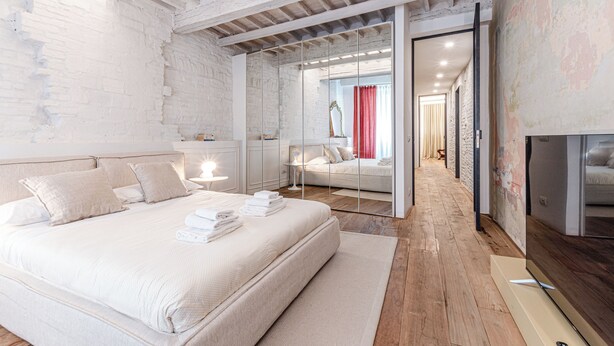 Une chambre moderne avec un grand lit, une cloison en verre et une vue sur une autre pièce.