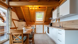 Une cuisine avec des poutres en bois, un coin repas avec une table et des chaises, et une fenêtre donnant sur un paysage agréable.