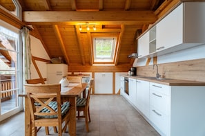 Une cuisine avec des poutres en bois, un coin repas avec une table et des chaises, et une fenêtre donnant sur un paysage agréable.