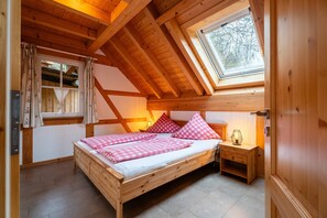 A wooden bedroom with a sloped ceiling, a skylight, a bed with pink checkered bedding, and a bedside table with a lamp. - Apartment 'Kronenhirsch' with Balcony and Wi-Fi (Oberharmersbach)