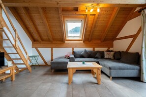 A loft-style room with a wooden ceiling, a gray sofa, a wooden coffee table, and a small table with a picture frame. - Apartment 'Kronenhirsch' with Balcony and Wi-Fi (Oberharmersbach)