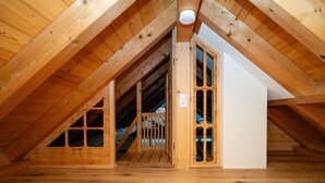 Une pièce mansardée avec des poutres en bois, un escalier et un mur blanc.