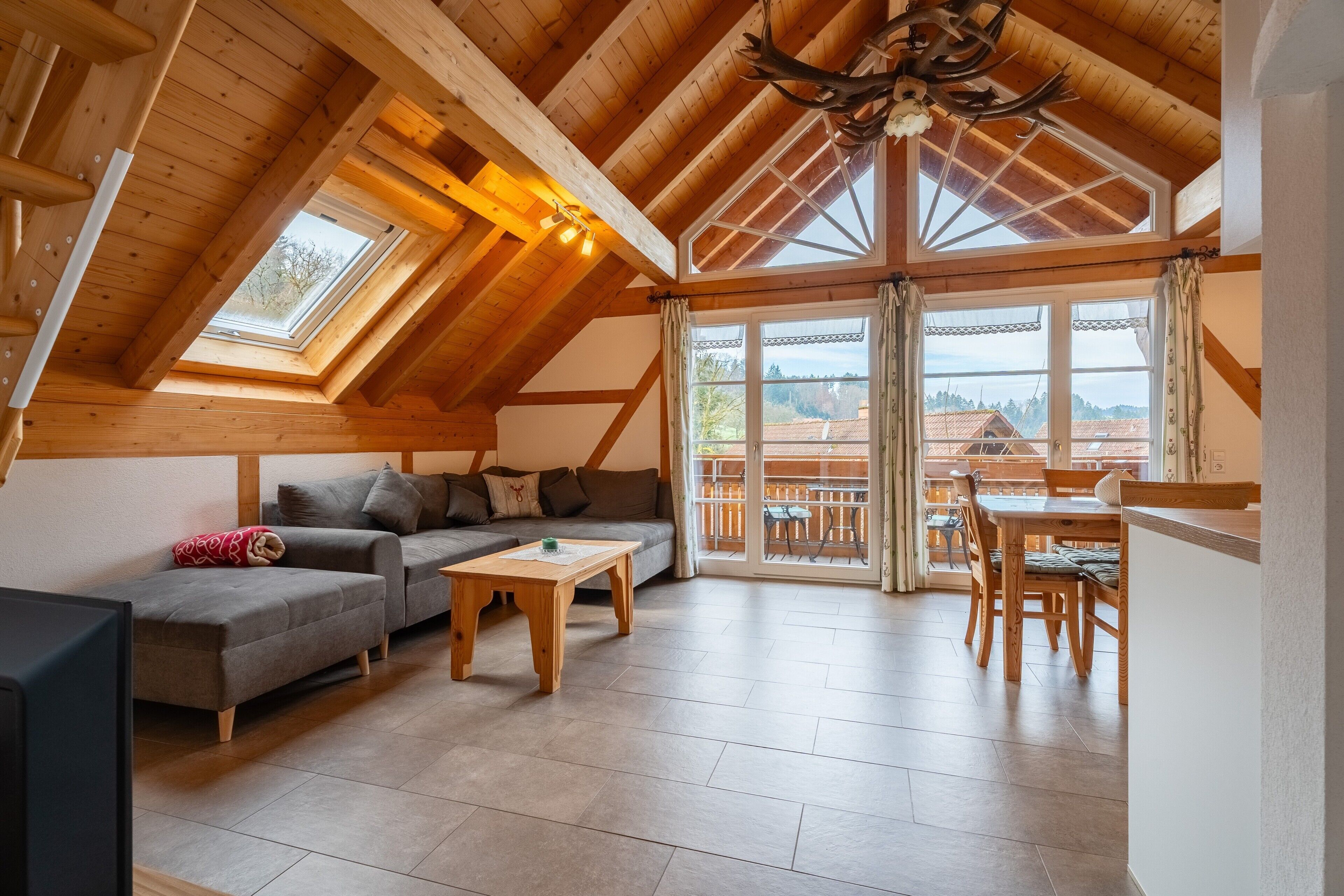 Ein geräumiges Loft mit Holzbalkendecke, einer Couch, einem Couchtisch und einem Essbereich mit Blick ins Freie.