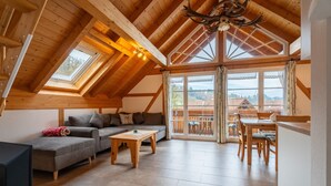 Un vaste espace de vie de style loft, doté d’un plafond en bois, d’un canapé, d’une table basse et d’un coin repas offrant une vue sur l’extérieur.