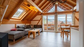 Ein geräumiges Loft mit Holzbalkendecke, einer Couch, einem Couchtisch und einem Essbereich mit Blick ins Freie.