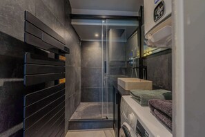 Ein modernes Badezimmer mit Duschabtrennung aus Glas, integriertem Waschbecken und Waschmaschine.