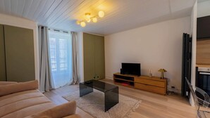 Ein modernes Wohnzimmer mit einer Couch, einem Glastisch, einem Fernseher auf einem Holzgestell und einem Kamin.