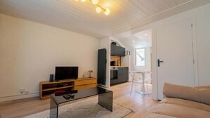 Ein modernes Wohnzimmer mit Flachbildfernseher, einer Holzunterhaltungsecke, einem Glastisch und einem beigefarbenen Sofa.