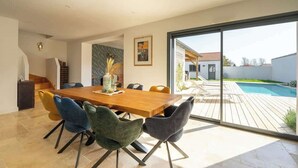 A modern dining area with a wooden table and colorful chairs, a large window, and a view of a swimming pool. - The Villa of the Waves (Châtelaillon-Plage)