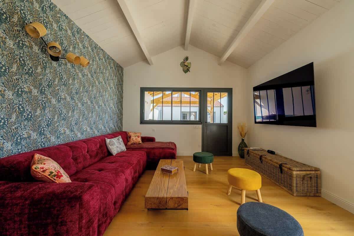 Een woonkamer met een rode bank, een houten salontafel en een geel poef.
