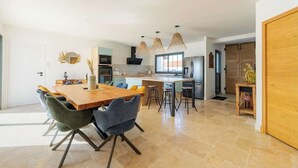 A spacious kitchen with a central island, modern pendant lighting, and a dining area with a wooden table and chairs. - The Villa of the Waves (Châtelaillon-Plage)