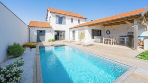 A swimming pool with a wooden deck, lounge chairs, and a covered outdoor area with a table and chairs. - The Villa of the Waves (Châtelaillon-Plage)
