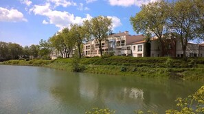 A multi-story residential building with balconies, situated beside a calm lake, surrounded by lush greenery. - Apartment - The Gentle Tides (La Rochelle)