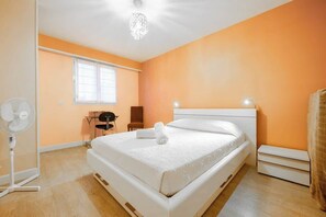 A bedroom with a bed, a desk, a chair, a standing fan, and a window. - Apartment - The Gentle Tides (La Rochelle)
