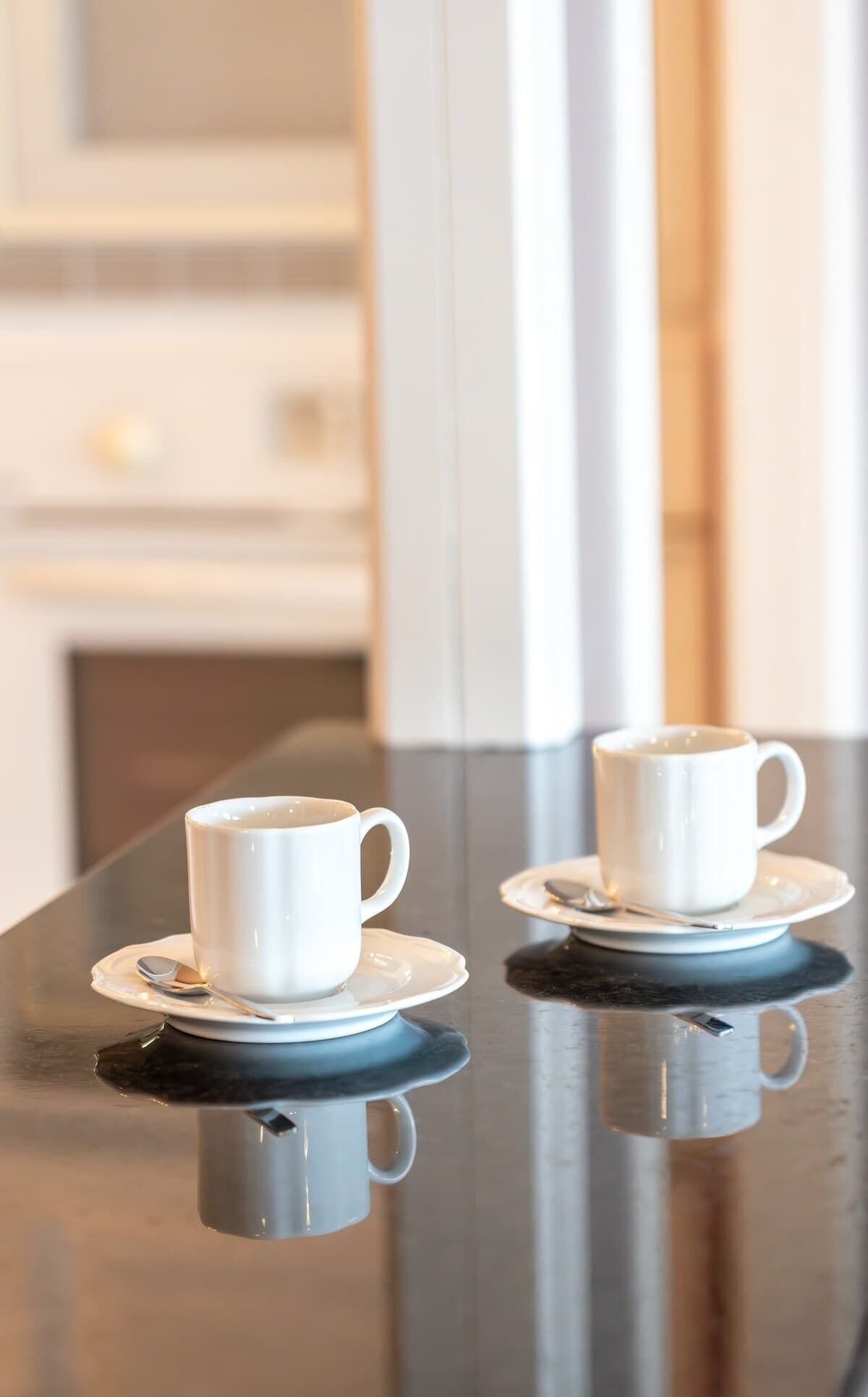 Two white cups on saucers on a reflective black table.