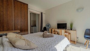 Ein Schlafzimmer mit Bett, Fernseher, Schreibtisch, Stuhl und Kleiderschrank.