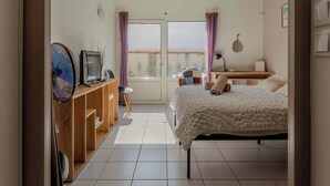 A bedroom with a bed, a desk, a chair, a fan, and a window with curtains. - Golden Waves Aparthotel - Kiwi Residence (Aytré)