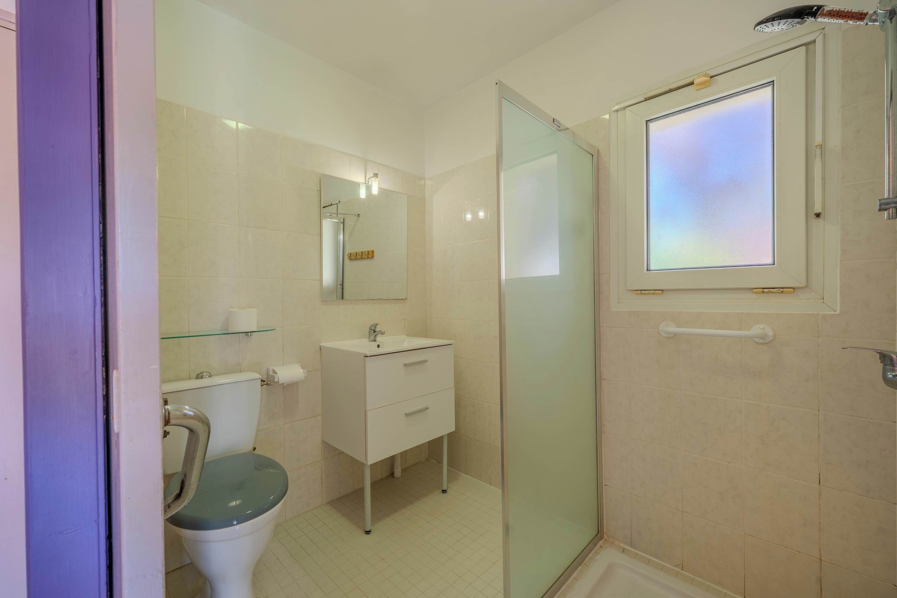 A bathroom with a toilet, sink, mirror, and shower.