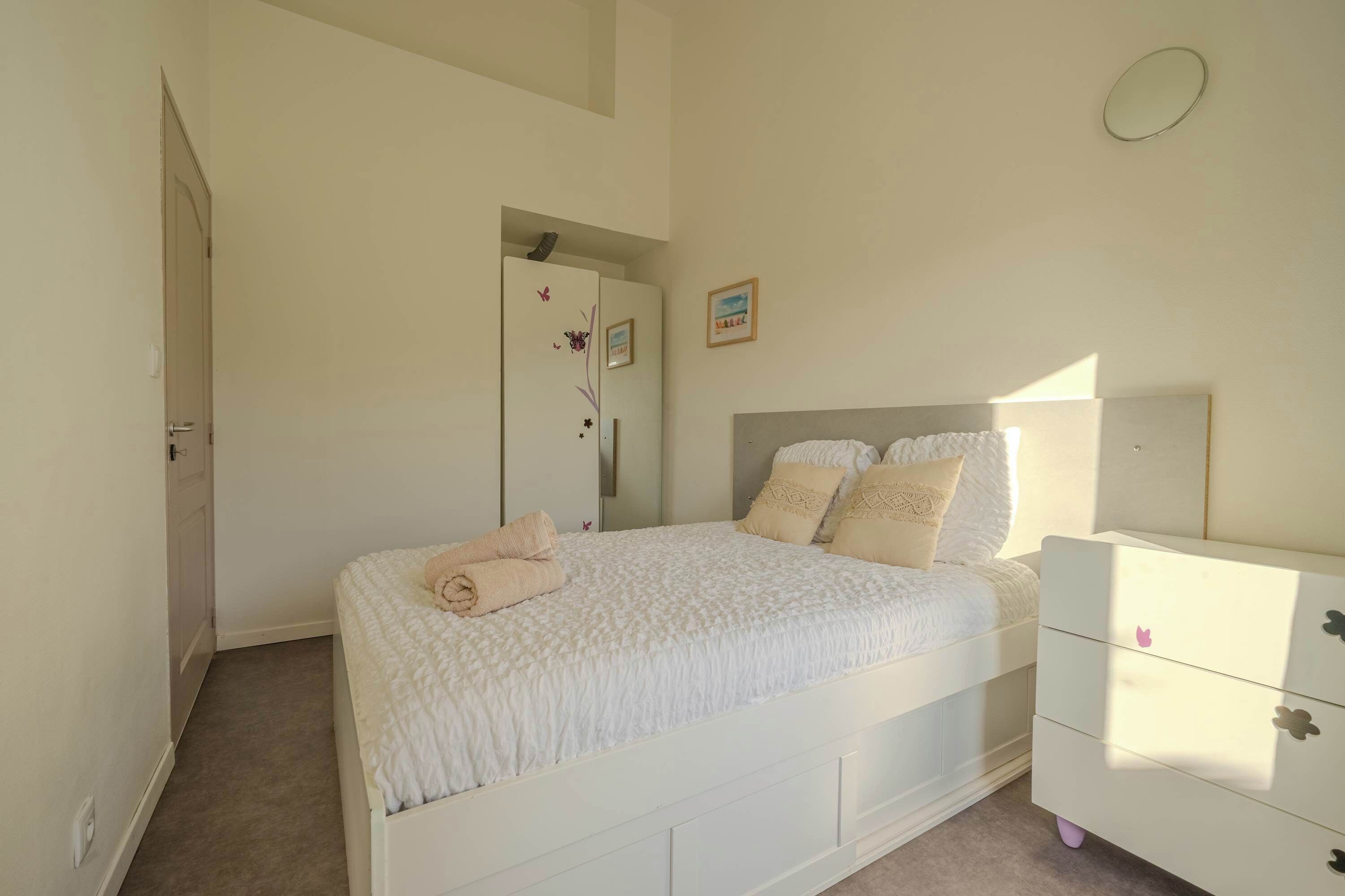 A bedroom with a bed, a dresser, a door, and a wall with a picture.
