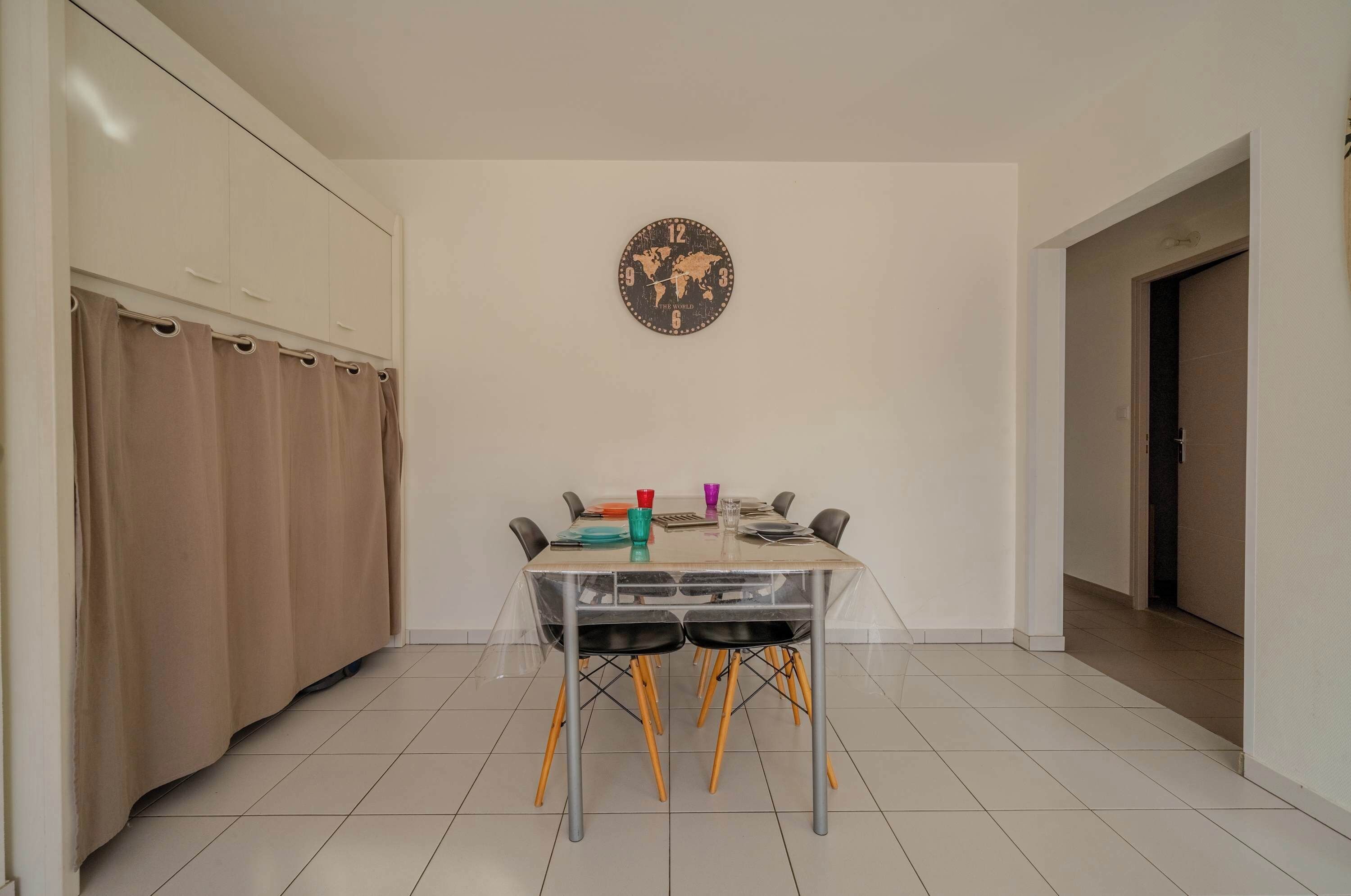 A dining area with a table, chairs, and a world map clock on the wall.