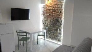 A compact kitchen with a TV, a small fridge, and a dining area with two chairs. - SageGreən Flat (Genova)