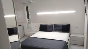 A bedroom with a bed, bedside tables, a mirror, and a wall-mounted air conditioner. - SageGreən Flat (Genova)