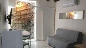 A room with a stone wall, a grey sofa, a small table, and a white door. - SageGreən Flat (Genova)