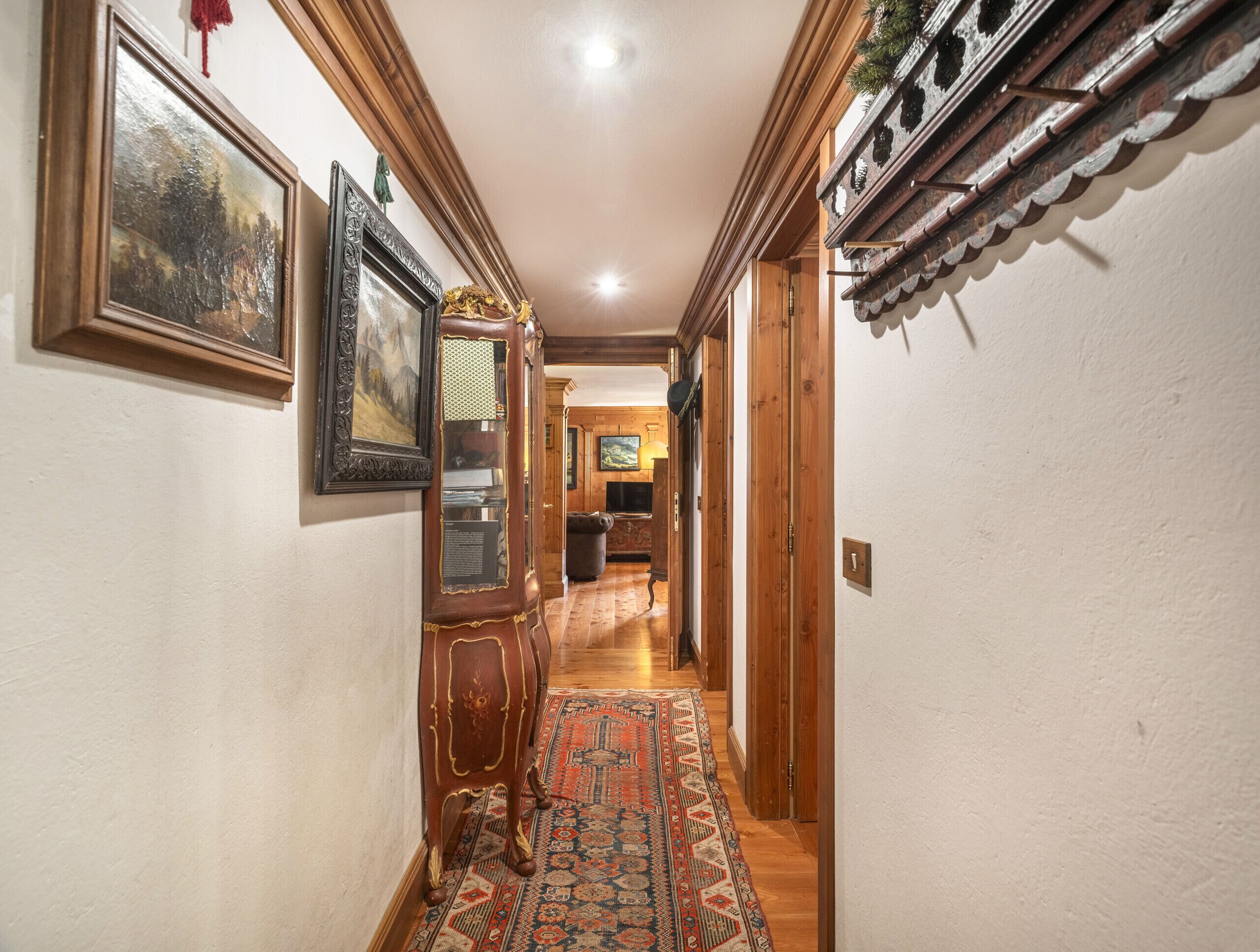A hallway with wooden doors, a patterned rug, and framed artwork on the walls.