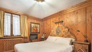A wooden-paneled room with a bed, a television, a nightstand, and a decorative headboard. - Angiolina Charming Apartment R&R (Cortina d´Ampezzo)