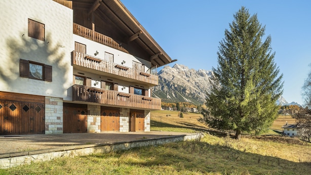 A two-story building with wooden balconies, stone walls, and a mountain backdrop. - Angiolina Charming Apartment R&R (Cortina d´Ampezzo)