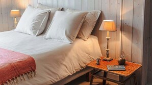 En pænt redt seng med hvide sengetøj og puder, et natbord med en lampe, en lille vase og en bog.