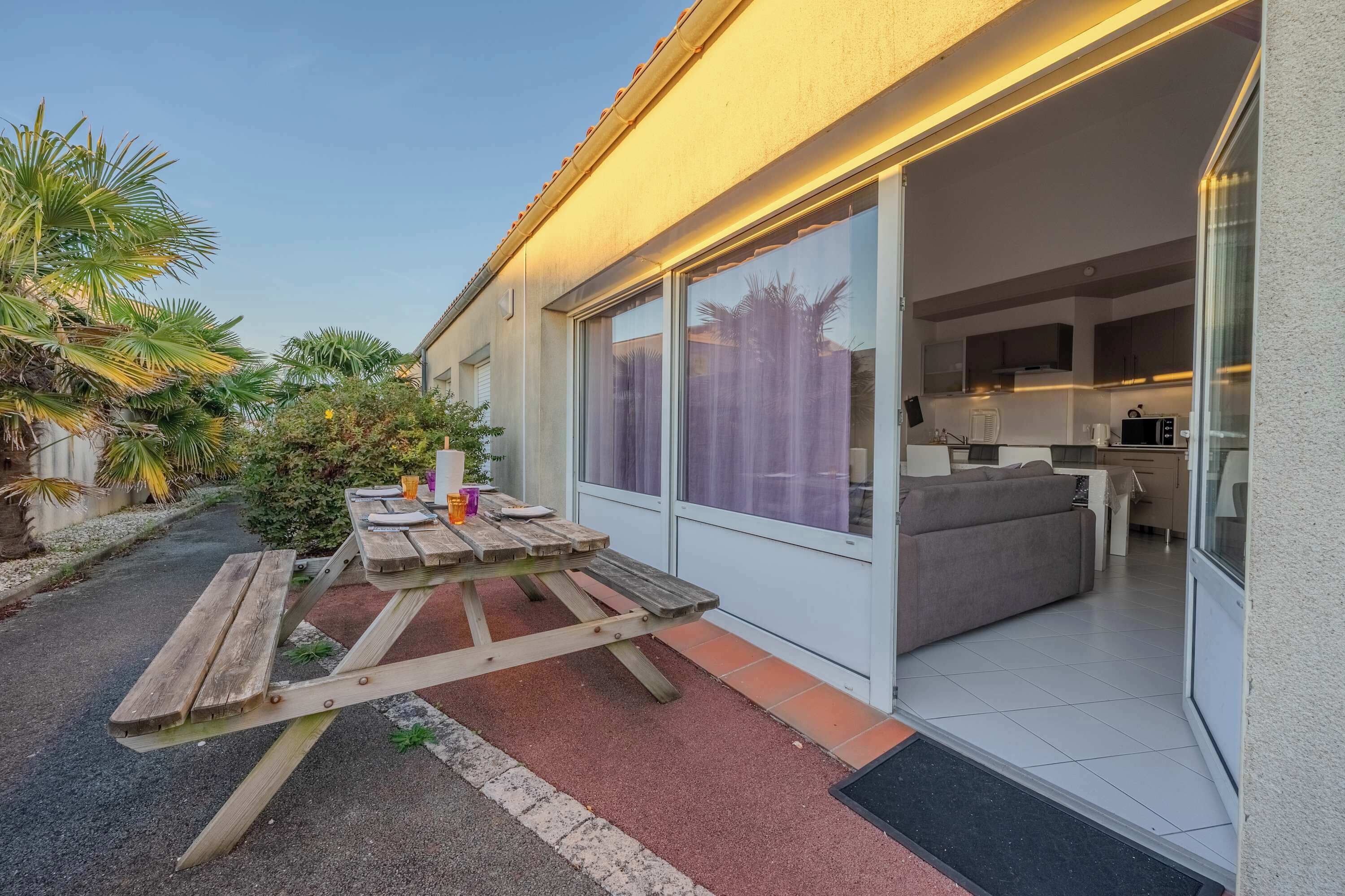 Une maison moderne dotée d’un patio, d’une cuisine ouverte sur le salon grâce à des portes vitrées et d’un petit jardin agrémenté de palmiers.