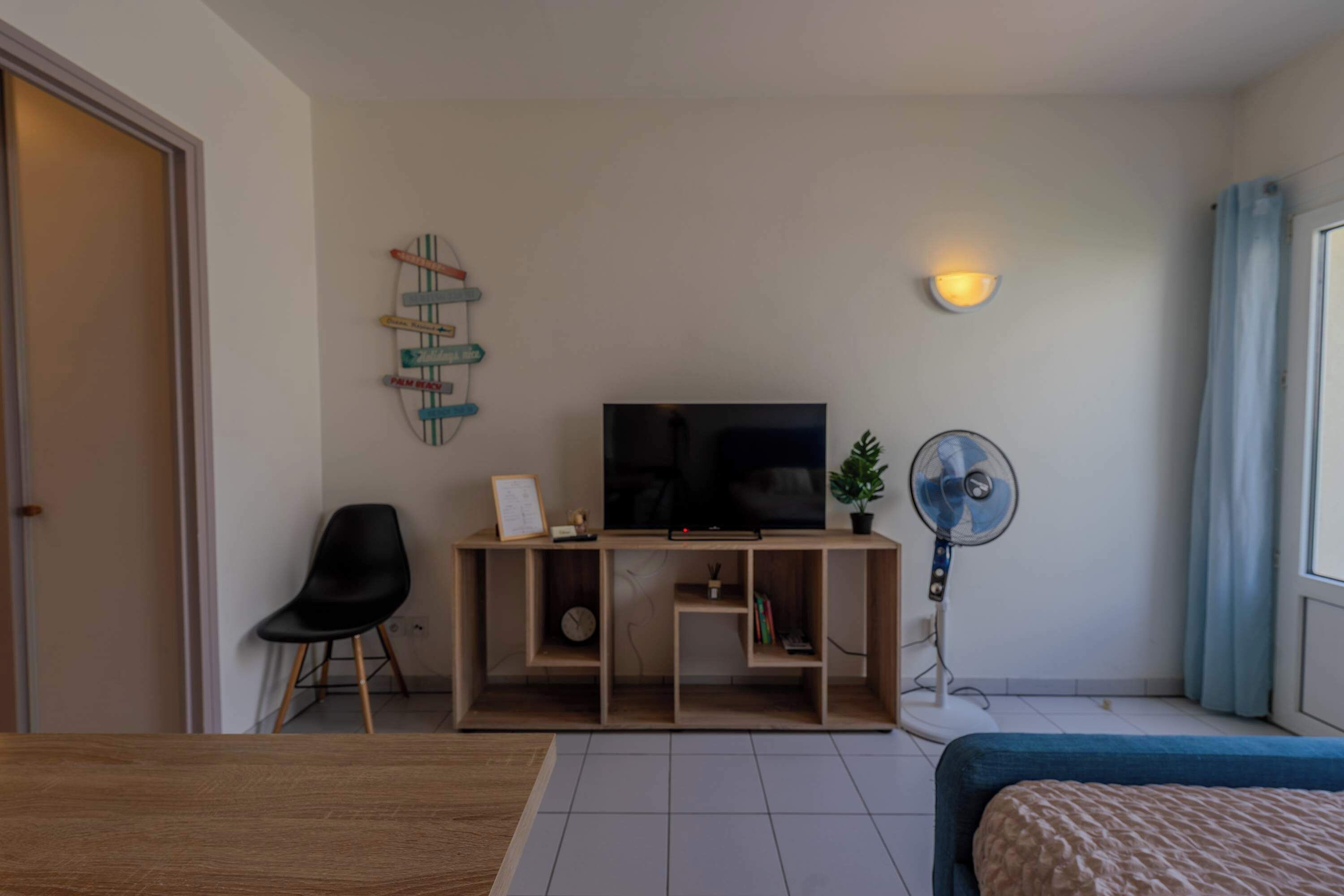 A modern room with a TV, a fan, a chair, and a bed.