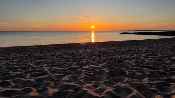 Une plage au coucher du soleil, avec le soleil qui se reflète sur l’eau.