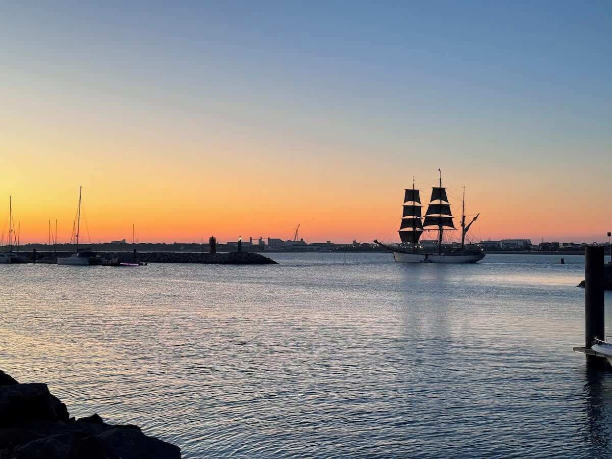 A sunset view of a harbor with a sailing ship and several smaller boats.