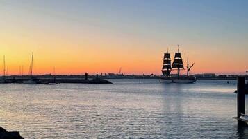 A sunset view of a harbor with a sailing ship and several smaller boats.