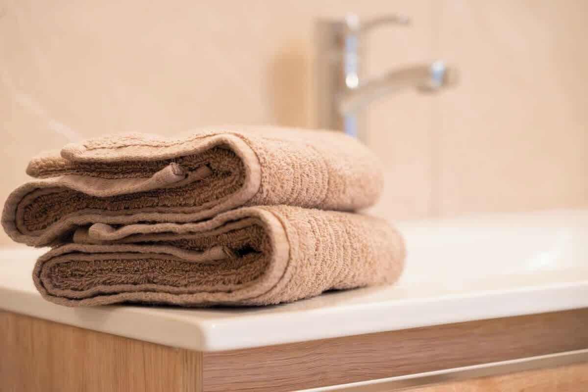 A stack of beige towels on a white bathroom sink.