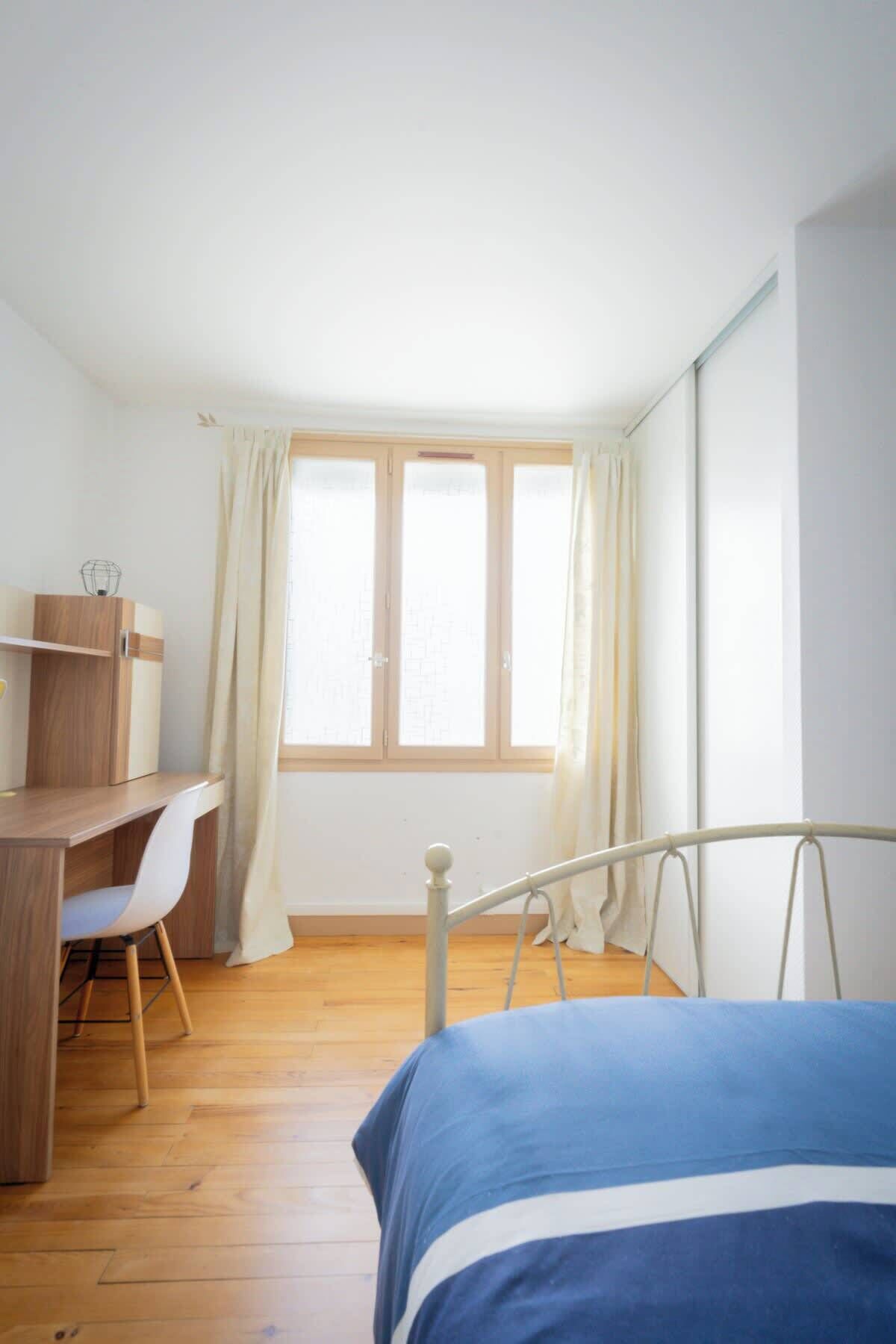 A bedroom with a bed, a desk with a chair, and a window with curtains.