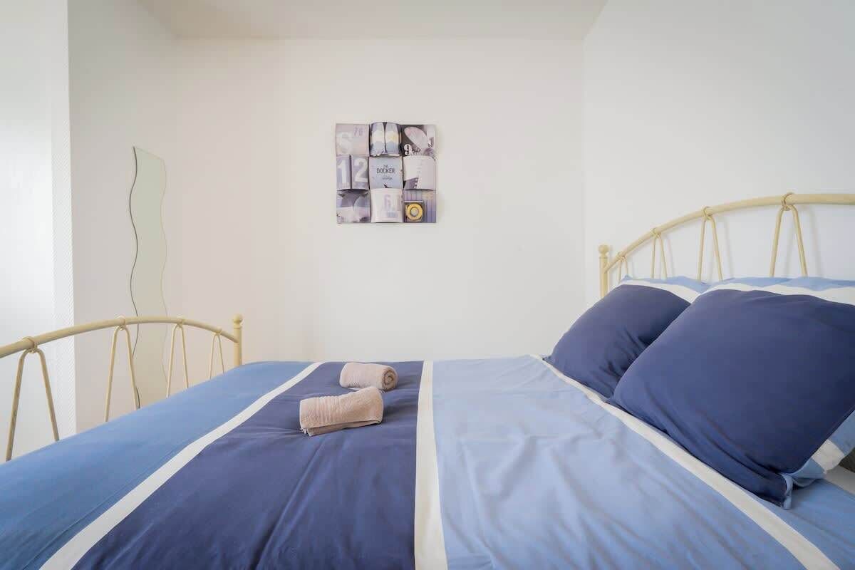 Ein ordentlich bezogenes Bett mit blau-weißer Bettwäsche, einem Holzkopfteil und einem an der Wand hängenden Kunstwerk.